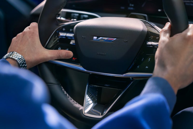 Close-up of a Man About to Press the V-Button on the 2026 OPTIQ-V Steering Wheel | Fitzgerald Cadillac of Hagerstown in Hagerstown MD