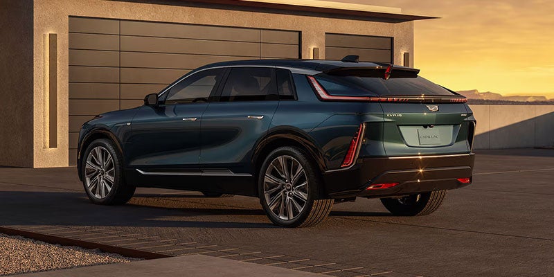 Dark green Cadillac SUV parked outside a modern home at sunset.