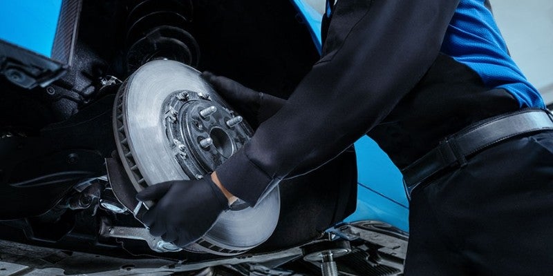 Auto service technician inspecting a vehicle's brake rotor and assembly.