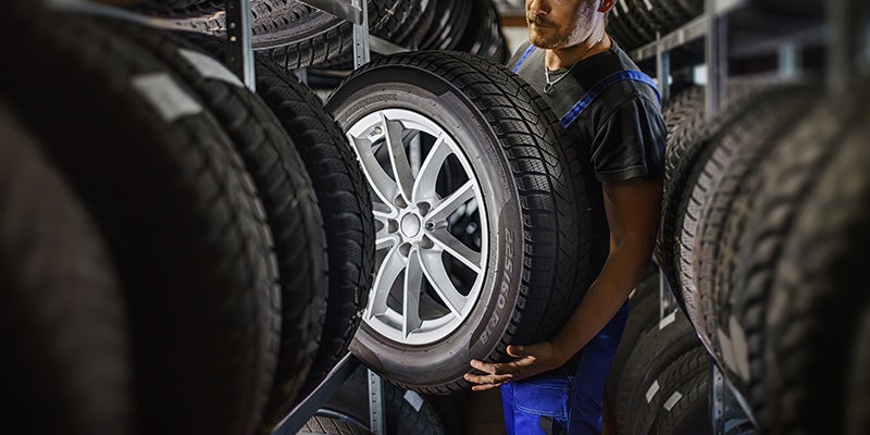 technician from Fitzgerald Cadillac of Hagerstown in Hagerstown MD carrying a tire